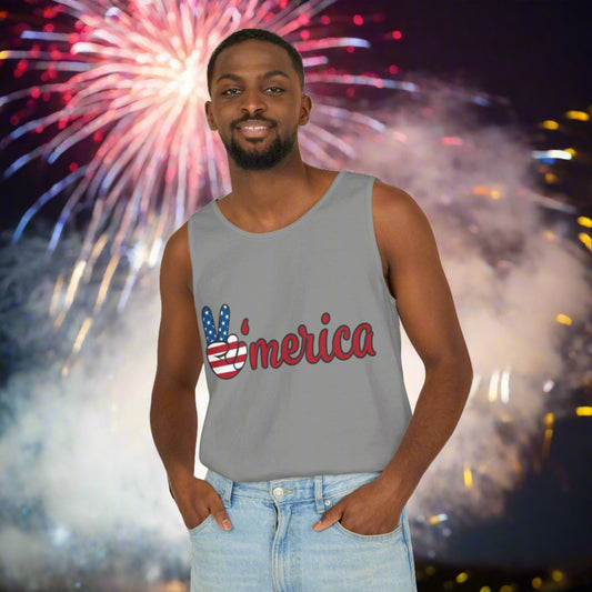 A man in a gray sleeveless shirt, a Printify Unisex Patriotic Tank-top: One color; Cotton; Relaxed-fit made from 100% US cotton with "America" in red, white, and blue lettering, stands in front of a dazzling fireworks display at night.