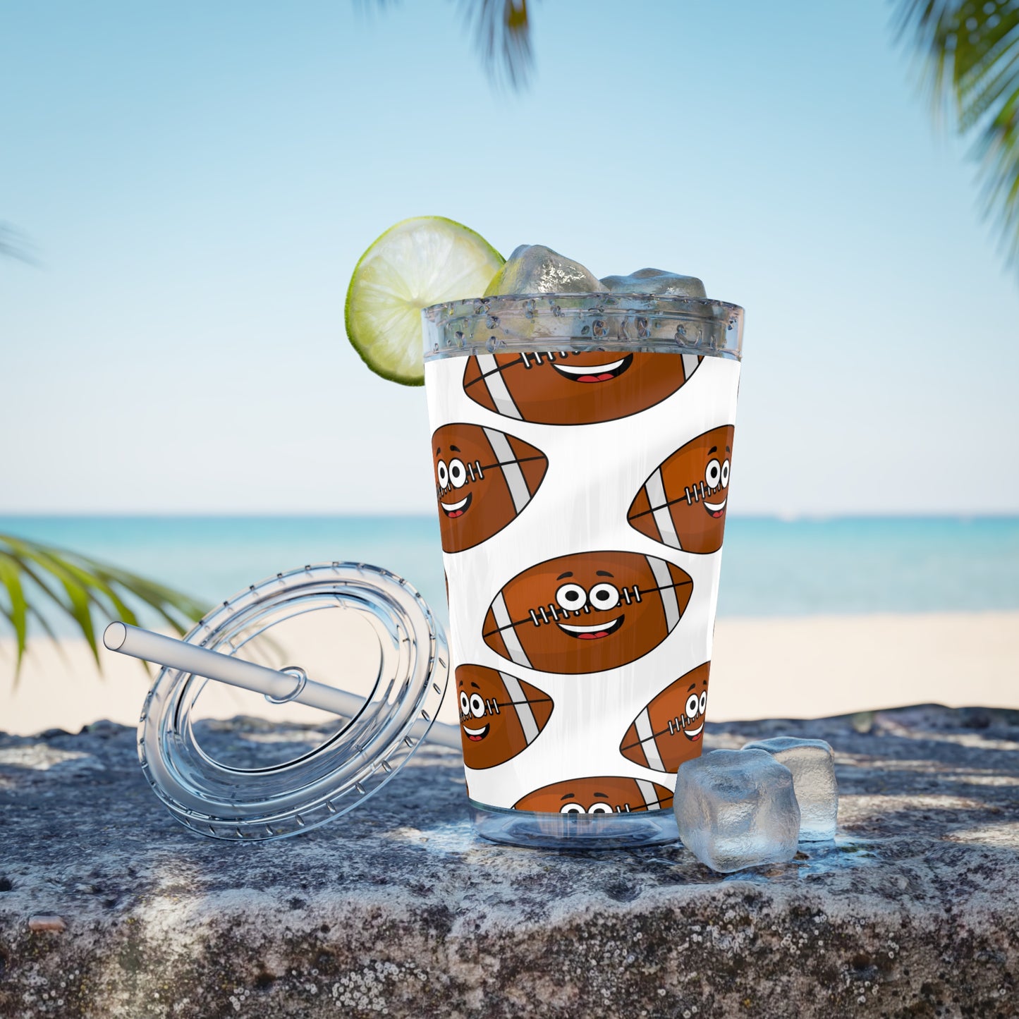 An American made Printify acrylic Football Fan Tumbler with a lime and a straw on the beach.