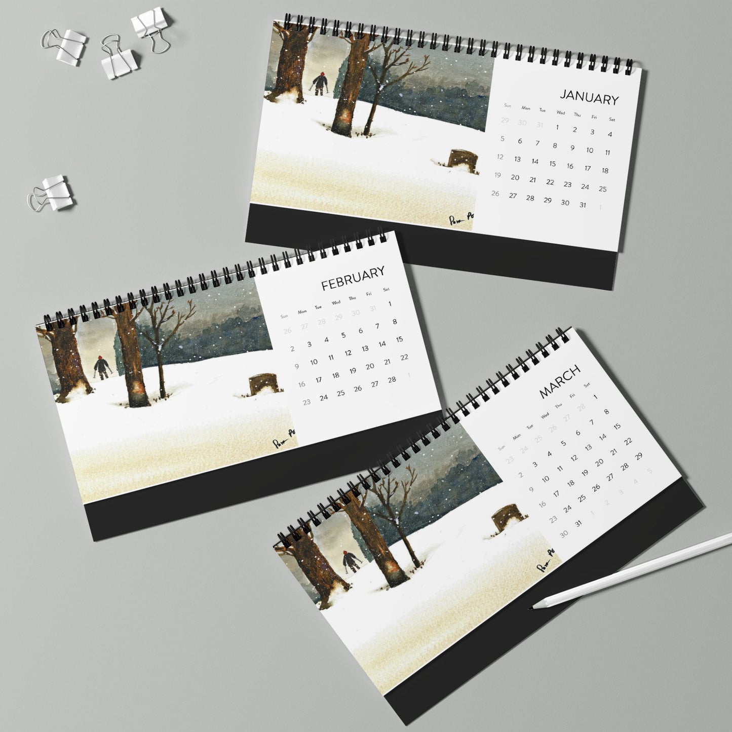 For nature enthusiasts, Printify's 2025 Desktop Calendar: Snowshoe Hiker showcases January, February, and March with stunning watercolor art of a snowy landscape and trees. A few paper clips and a white pen add to this tranquil arrangement.