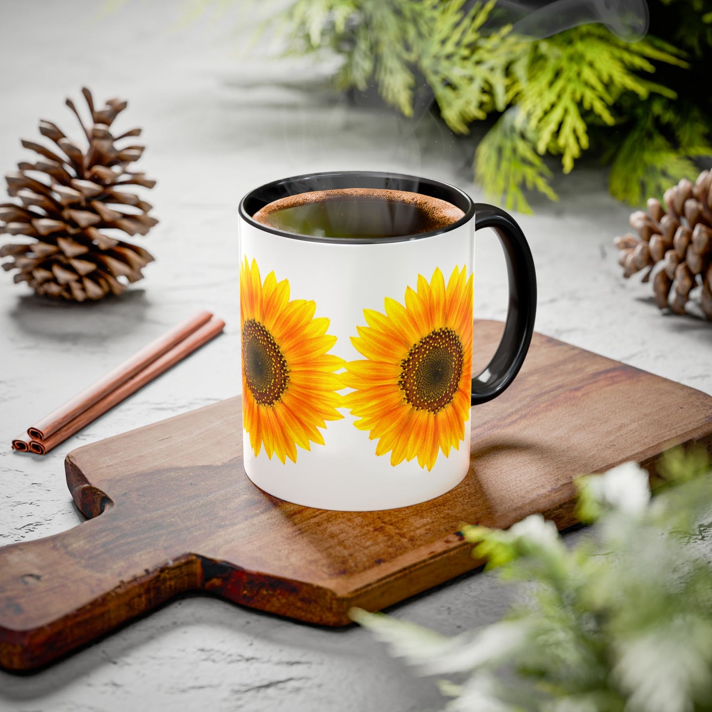 The Printify Sunflower Coffee Mug: Bright Floral (11oz, ceramic) sits on a wooden board with pinecones, cinnamon sticks, and greenery.