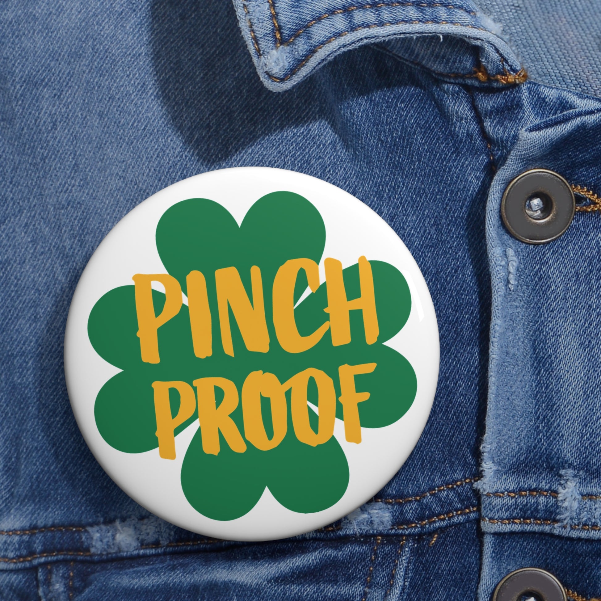 The Printify Metal Pin Button, available in 2 sizes, features a green shamrock and "PINCH PROOF" text—great for St. Patrick's Day and shown pinned on a blue denim jacket.