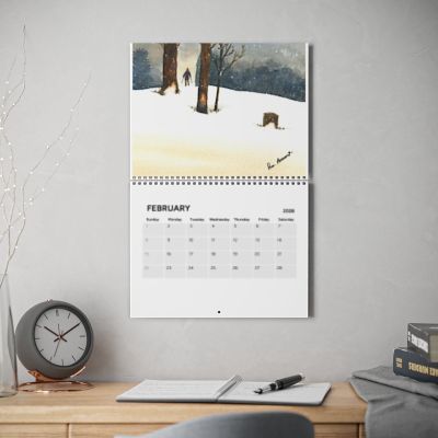 Calendar on a wall with a snowy landscape design, placed above a desk with stationery items.