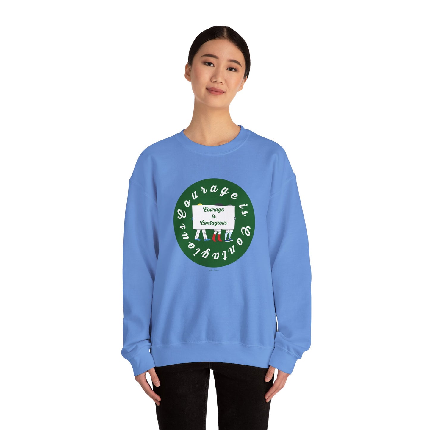 A woman wears the Printify Unisex Crewneck Sweatshirt: Courage is Contagious | Protest in light blue with a green and white “Courage is Contagious” graphic, standing against a plain white background—perfect for daily inspiration.