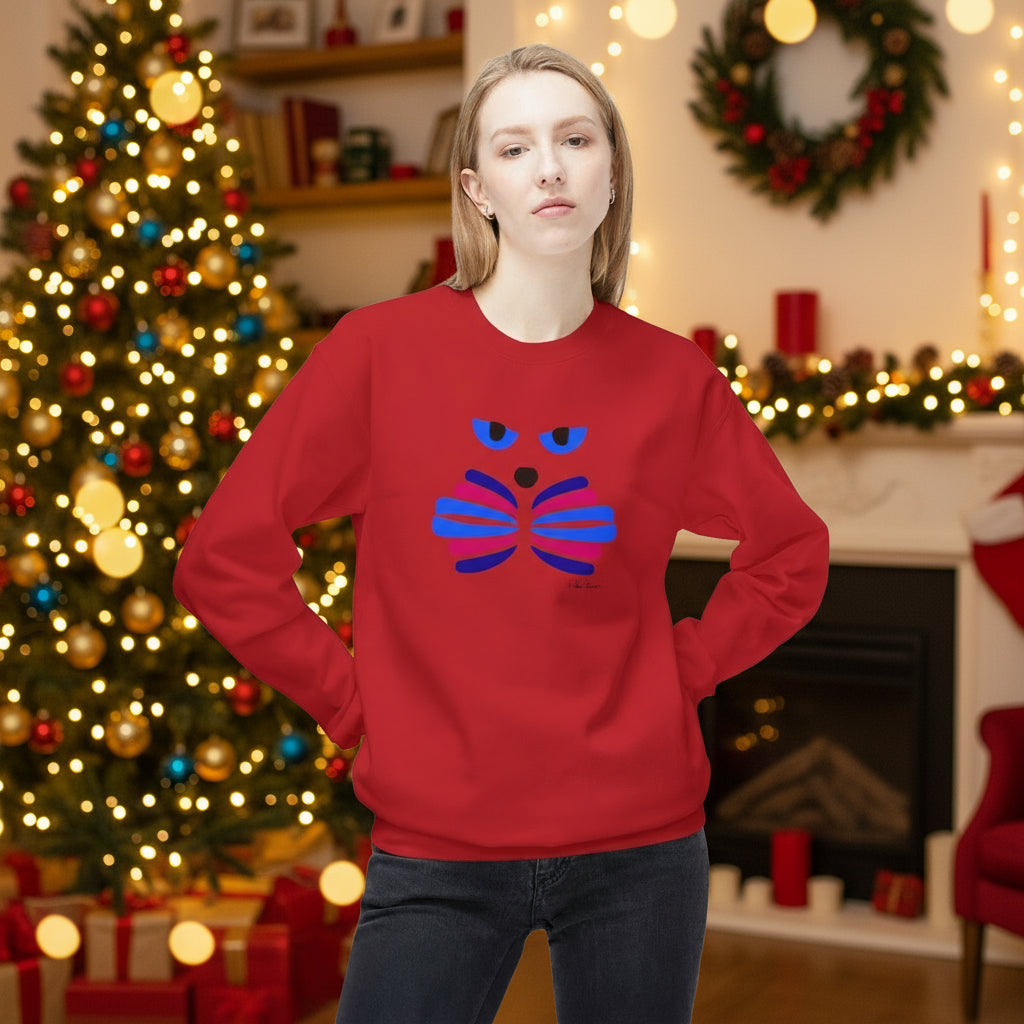 A woman stands indoors wearing the Printify Cat Face Crewneck Sweatshirt: Abstract Red & Blue Kitty; behind her are a decorated Christmas tree, wreaths, and a lit fireplace.