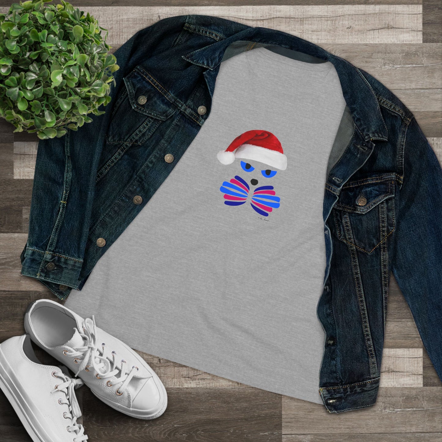 Printify Festive Women's Santa-Cat T-shirt in soft cotton, available in 2 cute colors, styled playfully with a denim jacket, white sneakers, and a potted plant on a wooden floor—perfect for the holidays!.