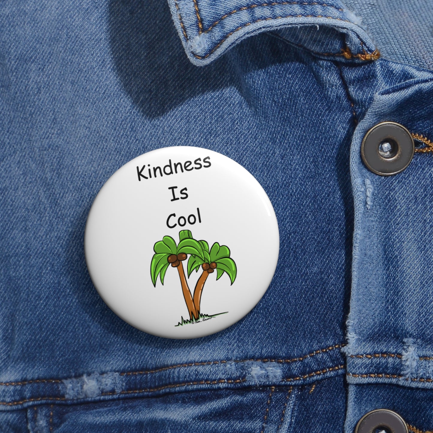 A round Unisex Kindness-Is-Cool Button by Printify, available in 2 sizes and featuring an illustration of two palm trees, is pinned to a denim jacket. This lightweight metal accessory with a safety pin backing adds a positive vibe to any outfit.