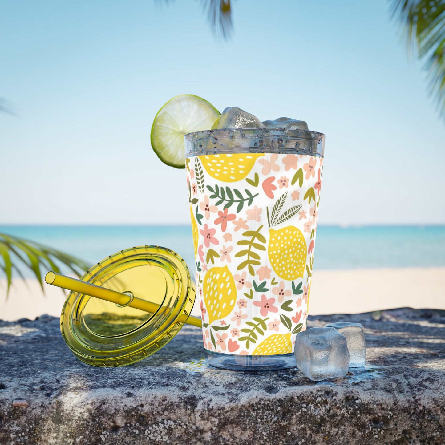 A Printify BPA-free Pink Lemons Tumbler of lemonade with a lime and a straw on the beach.