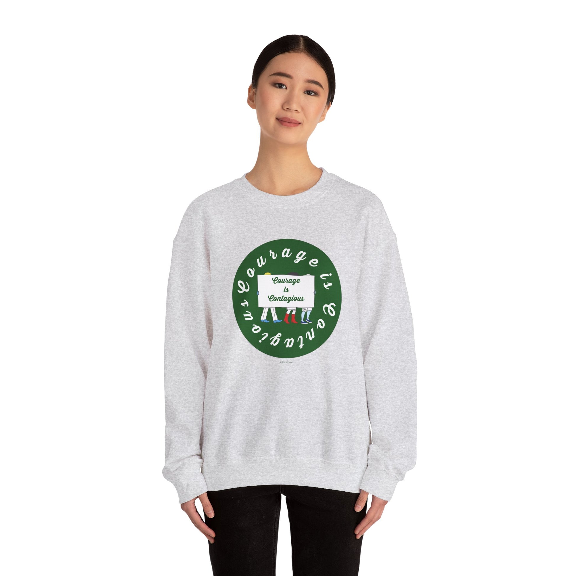 A woman wears the Printify Unisex Crewneck Sweatshirt: Courage is Contagious | Protest, featuring a light gray color, green circular design, and white "Courage is contagious" text, standing facing forward against a white background.