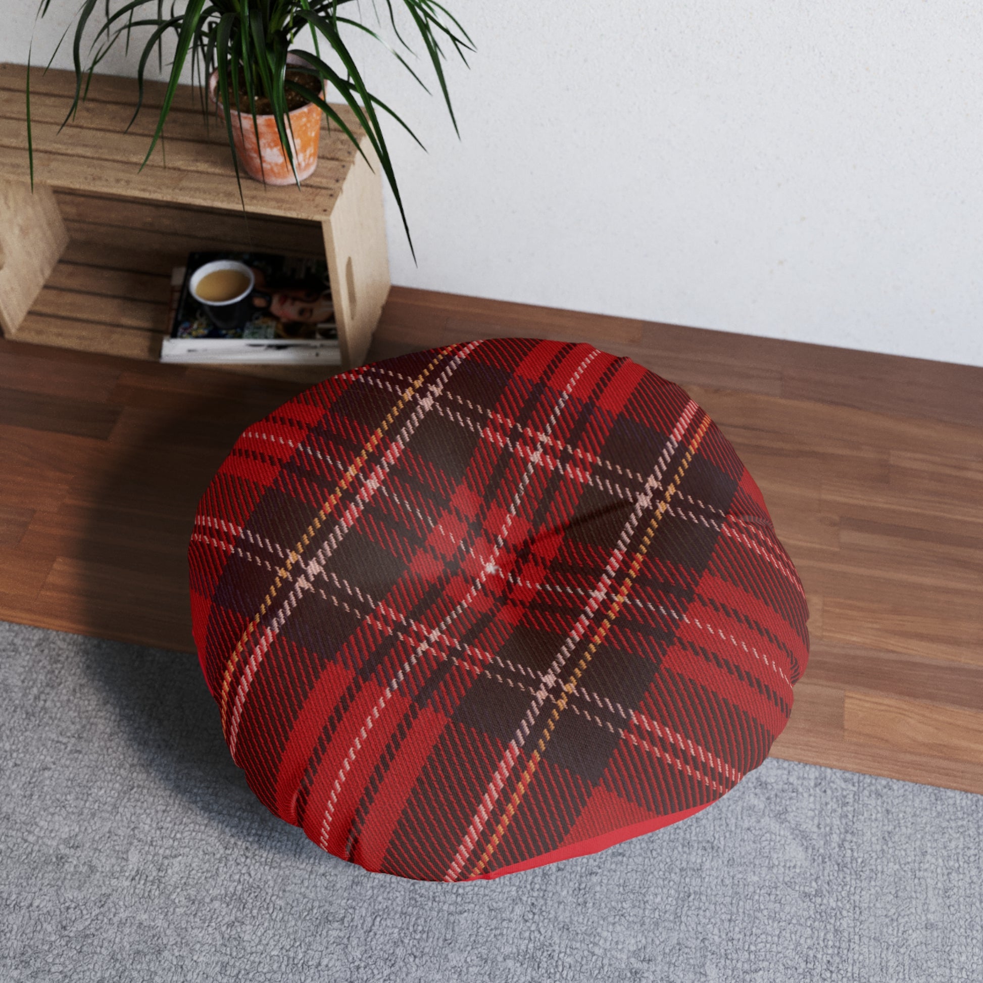 A comfortable Printify plaid tufted floor-pillow sits on a wood floor next to a plant.