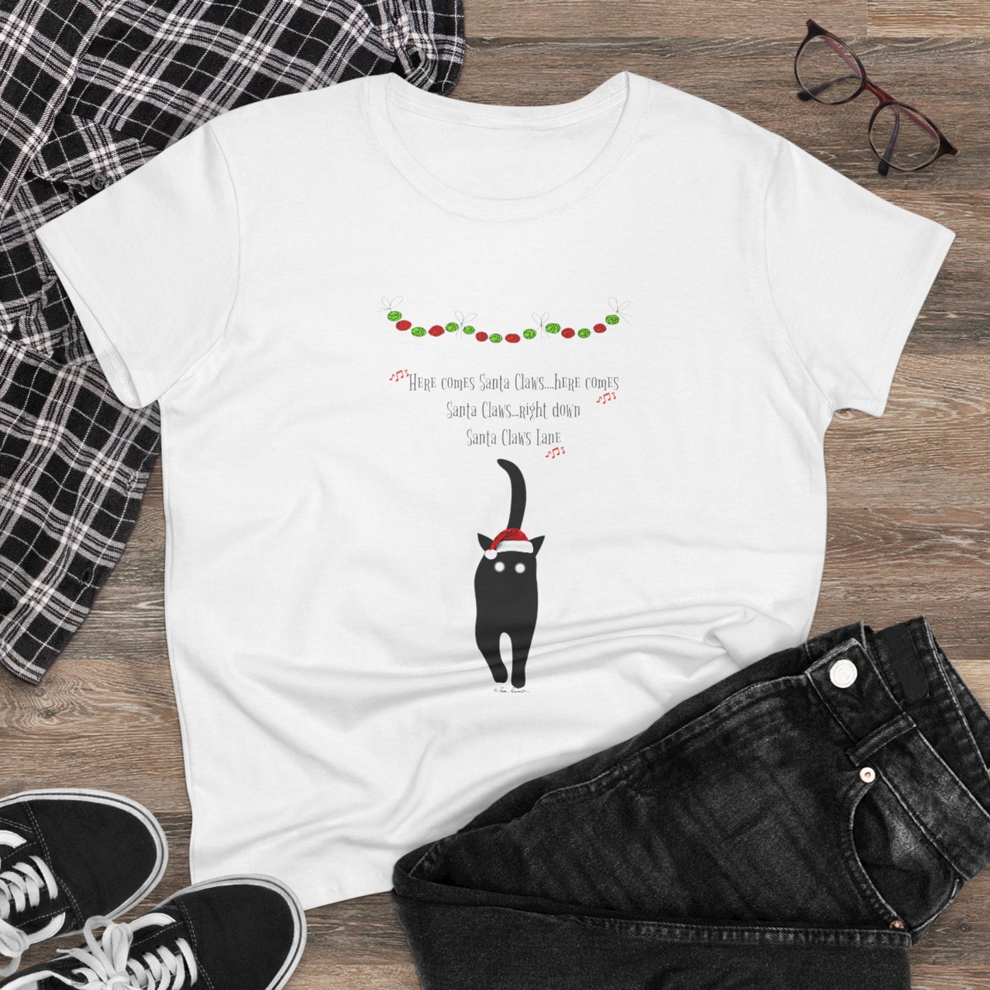 The Santa Claws T-shirt by Printify, a festive and playful women’s cotton tee featuring a cartoon black cat in a Santa hat and holiday lights, is the perfect holiday shirt to style with black jeans and sneakers this season.