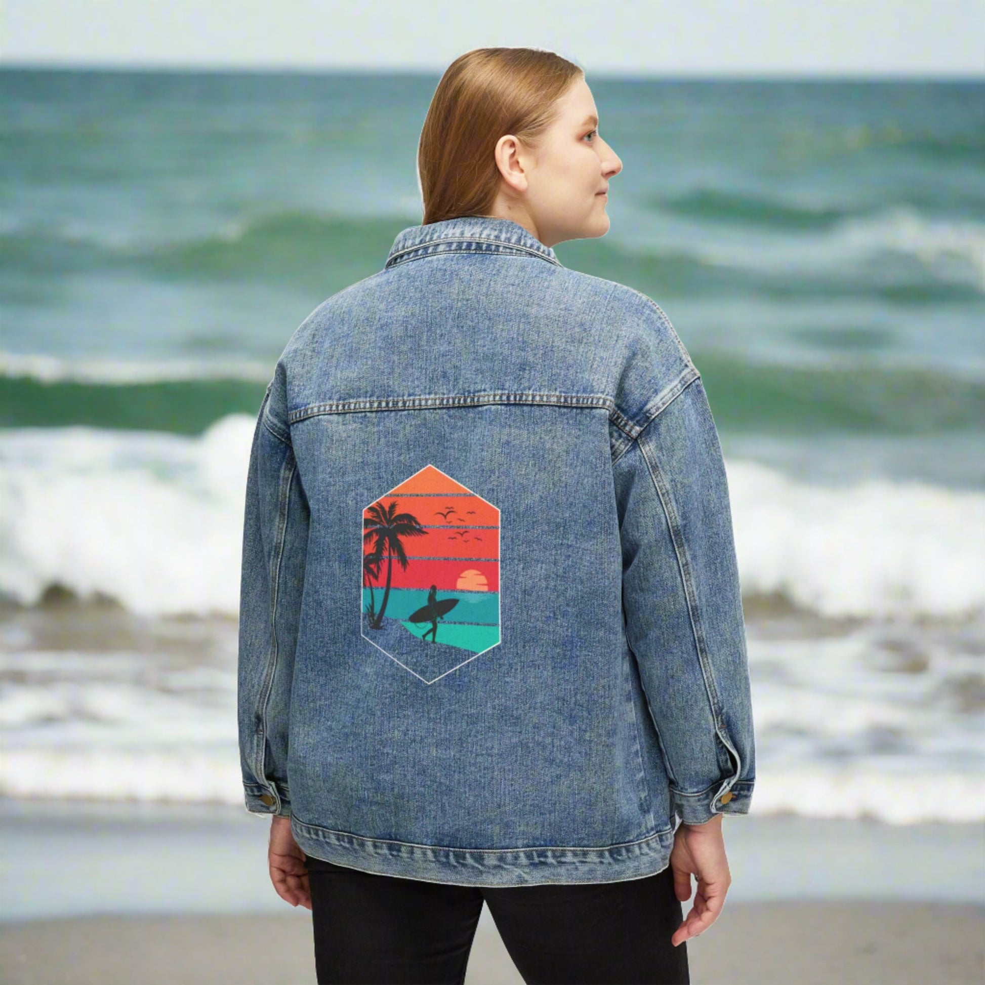 Woman wearing an oversized Printify Surfer-Girl Denim Jacket with a colorful tropical beach graphic on the back.