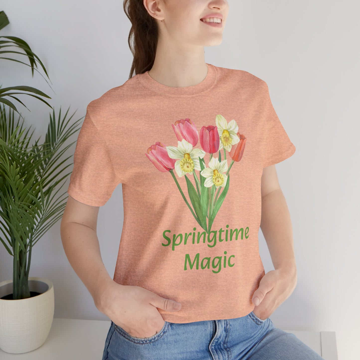 Woman wearing a peach-colored cotton Unisex Springtime-Magic T-shirt from Bella + Canvas by Printify with a spring-themed graphic artistry and the phrase "springtime magic.