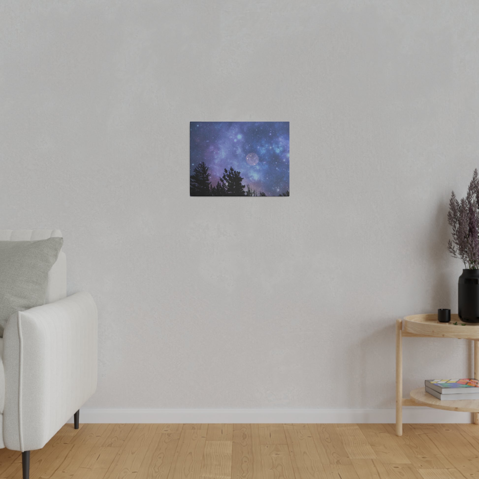 A Printify Blue-Moon Matte Canvas depicting a starry night sky, encased in a radial pine frame sourced from renewable forests, hangs on a plain wall in a room with a sofa and a wooden side table.