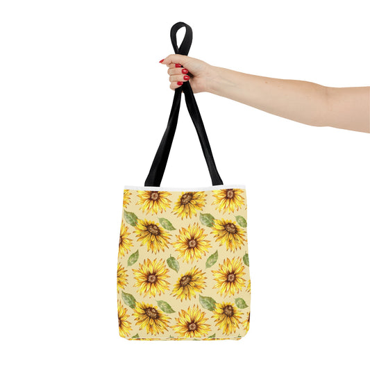 Sentence with product replaced: A hand with red nail polish holding a Printify polyester tote bag with a yellow sunflower print against a white background.