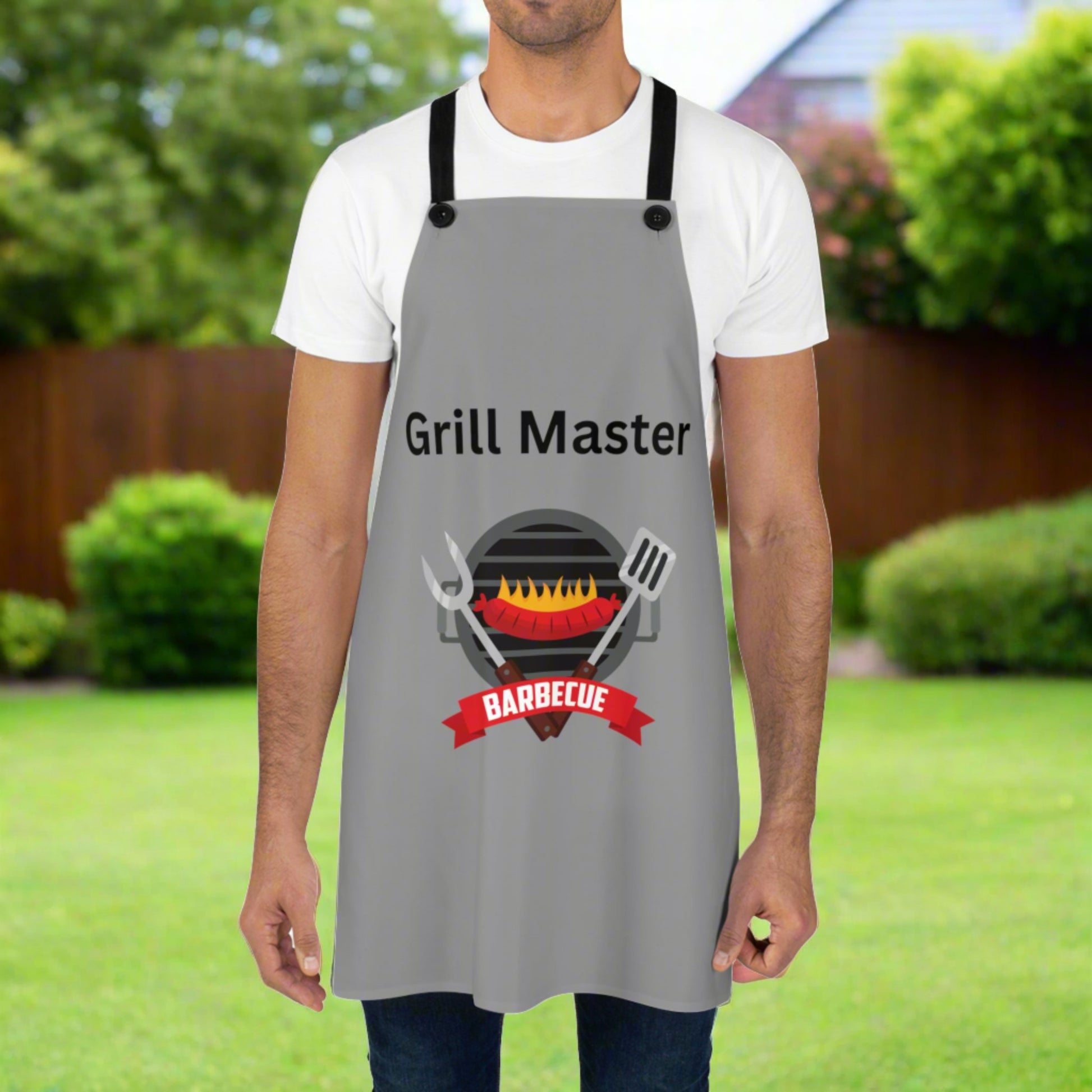 A person stands in a backyard, proudly wearing a gray USA-made Grill Master Apron: Unisex; Polyester; Lightweight; Graphics by Printify with "Grill Master" and a barbecue grill graphic—a perfect grilling gift for any barbecue enthusiast.