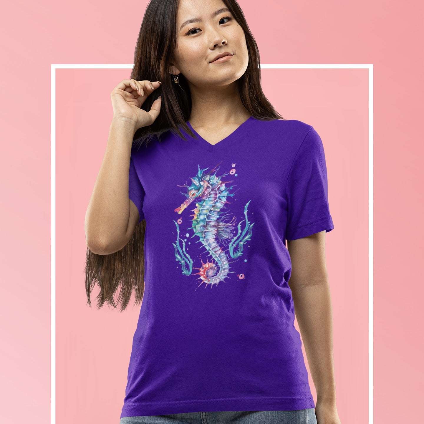 A person in a Printify Bella+Canvas cotton Unisex V-neck T-shirt, featuring a colorful seahorse design in a floral setting, poses against a pink background and white square border.