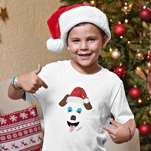 Wearing a Festive Santa-Dog Kids T-shirt by Printify and a Santa hat, a child joyfully poses in front of a beautifully decorated Christmas tree, embodying the spirit of holiday cheer.