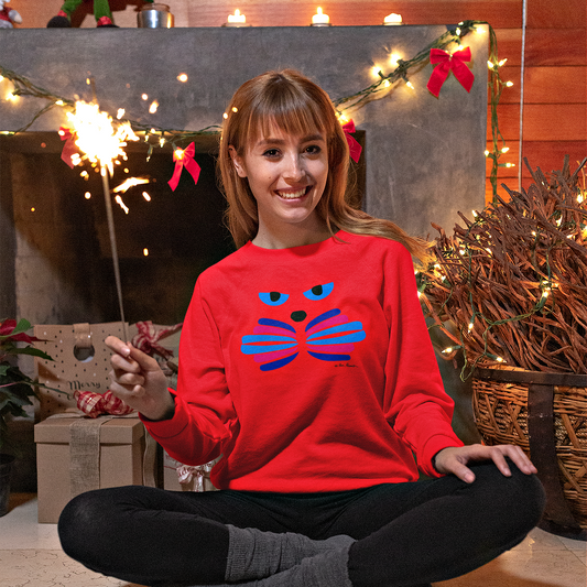 Wearing a Printify Unisex Cat-Art Sweatshirt, which is proudly made in America and comes in three color options, a woman holds a sparkler while sitting cross-legged on the floor in front of a festively decorated fireplace.