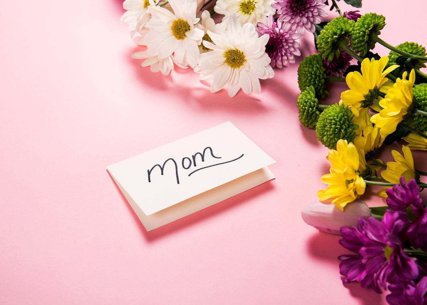 Photo of flowers and a gift card with text which reads "Mom" on the front of it
