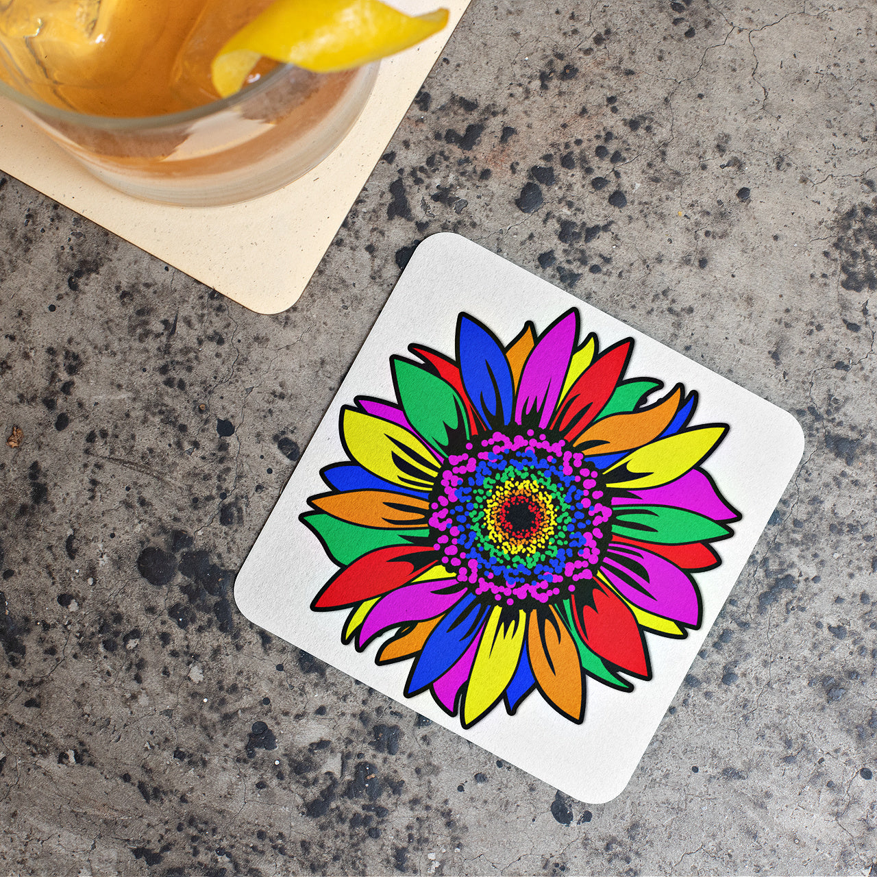 Mock up of one of the Rainbow Sunflower Coasters next to a cocktail over a concrete surface