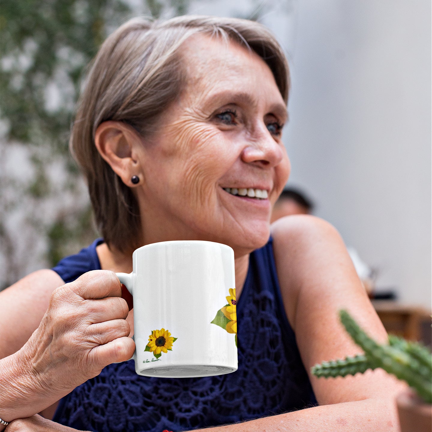 Mock up of a smiling woman with the left side of our Sunflower Ceramic Mug visible