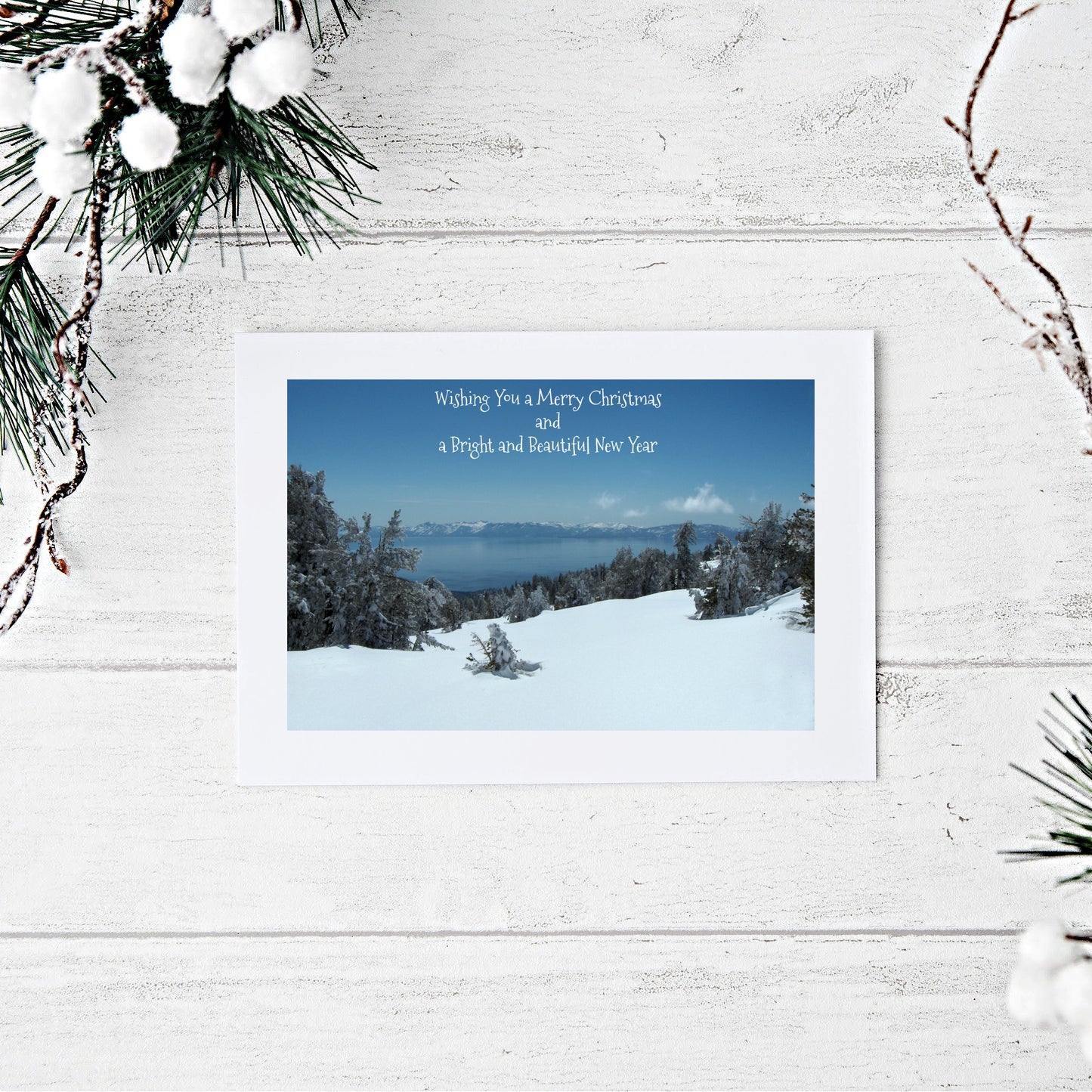 Mockup of our Merry Christmas Card featuring a snow scene with blue Lake Tahoe in the distance and a  printed greeting above