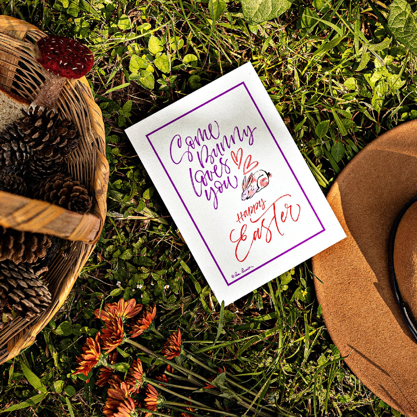 Mock up of our Easter Greeting Card lying on the grass next to a basket and hat