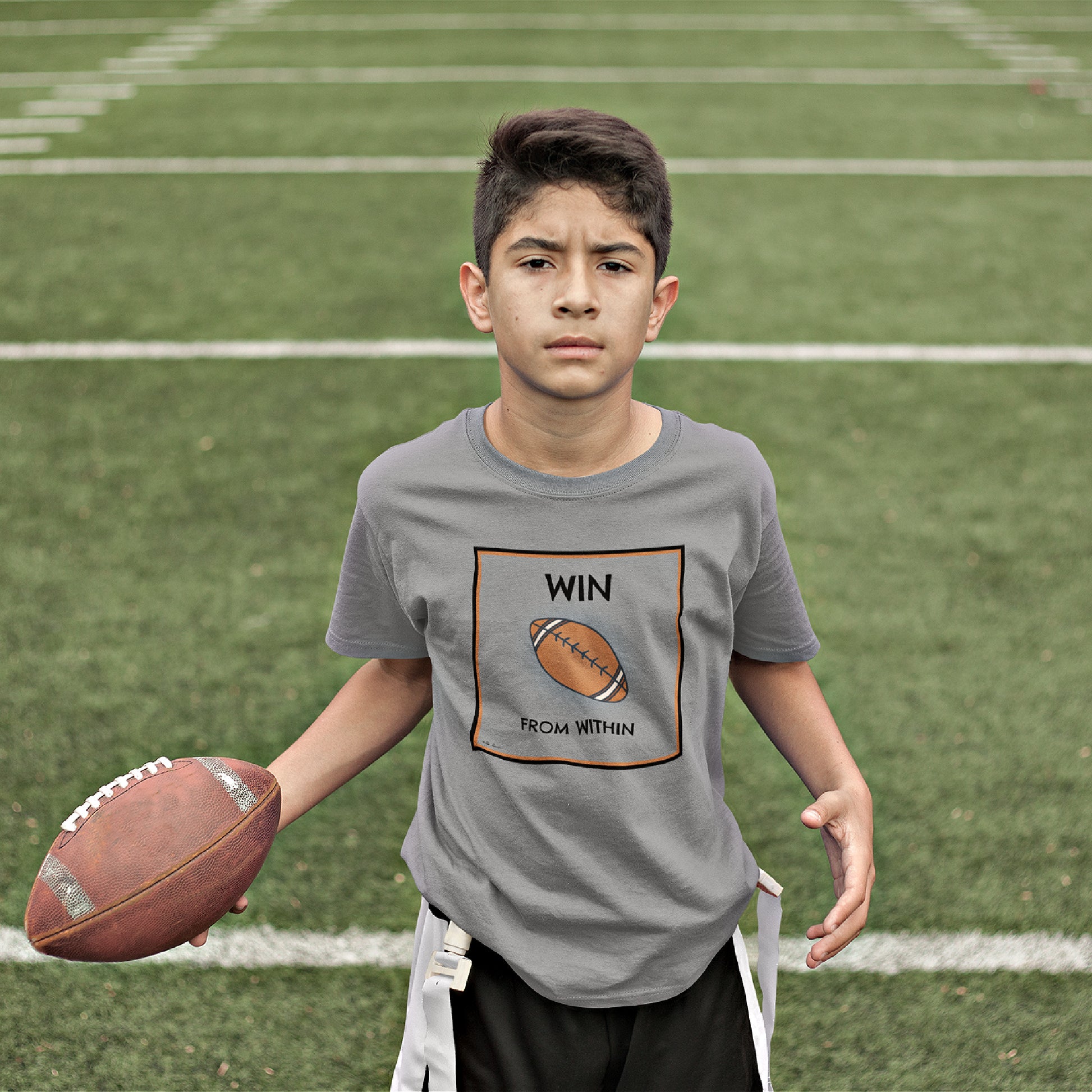 Mock up of a boy holding  a football while wearing our T-shirt