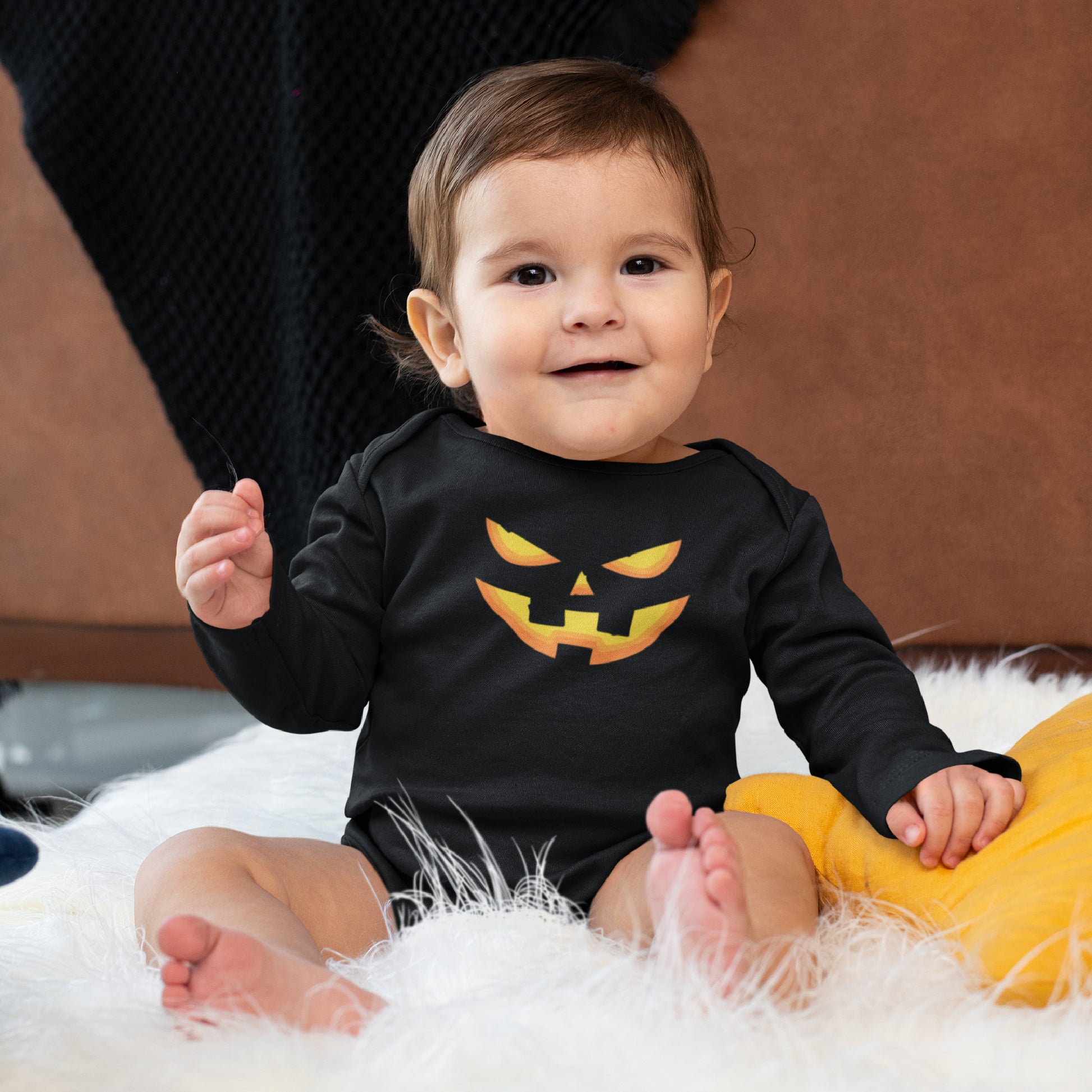 Mock up of a baby boy wearing a black long-sleeve onsie featuring a smiling Pumpkin Face