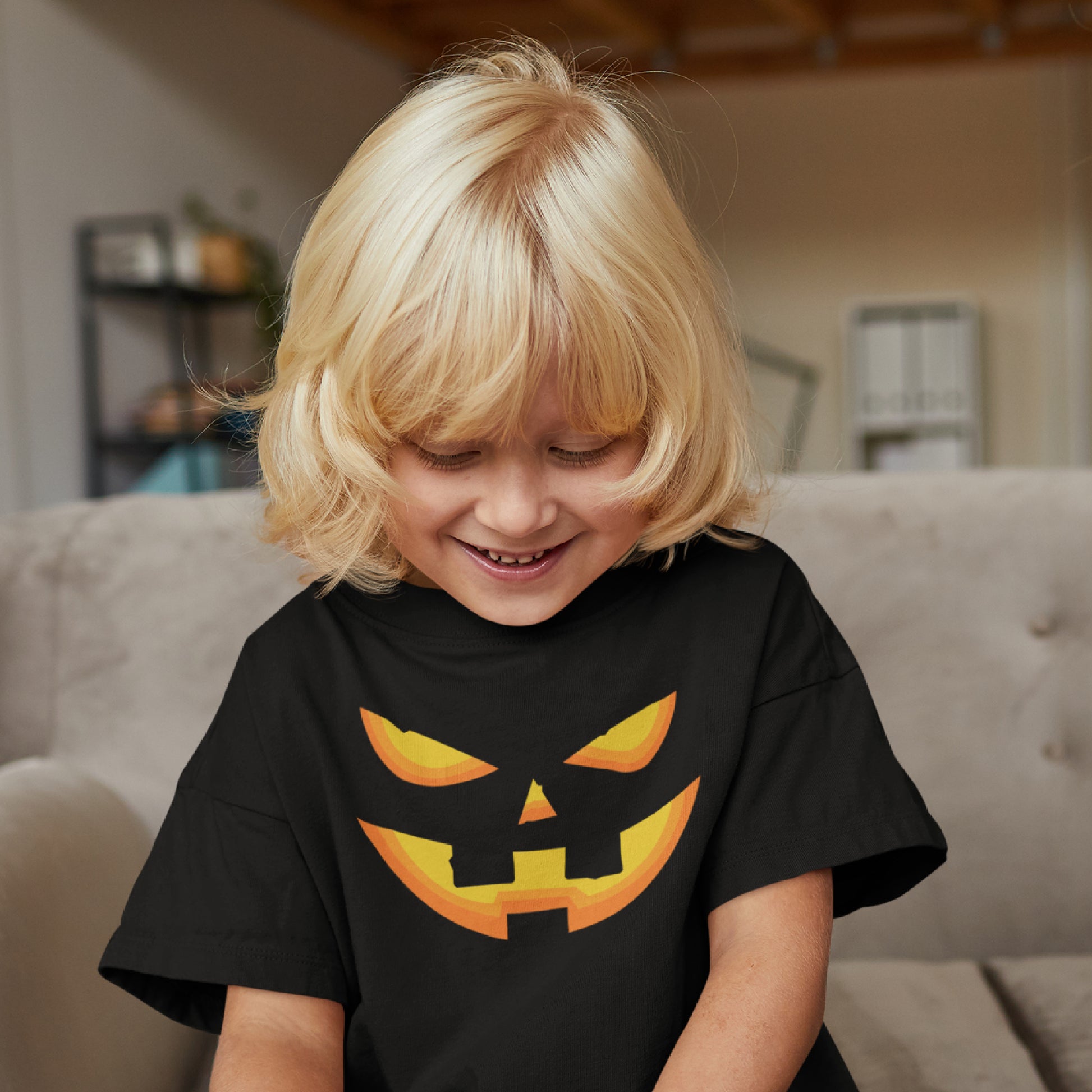 Mock up of a little girl with blond hair who is smiling and wearing our black Kids Halloween T-shirt featuring a Pumpkin Face.