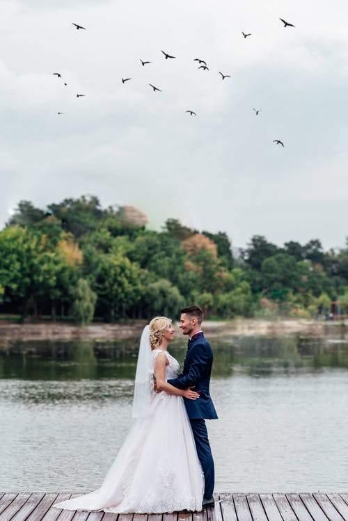 Photo of a bride and a groom standing next to a body of water 